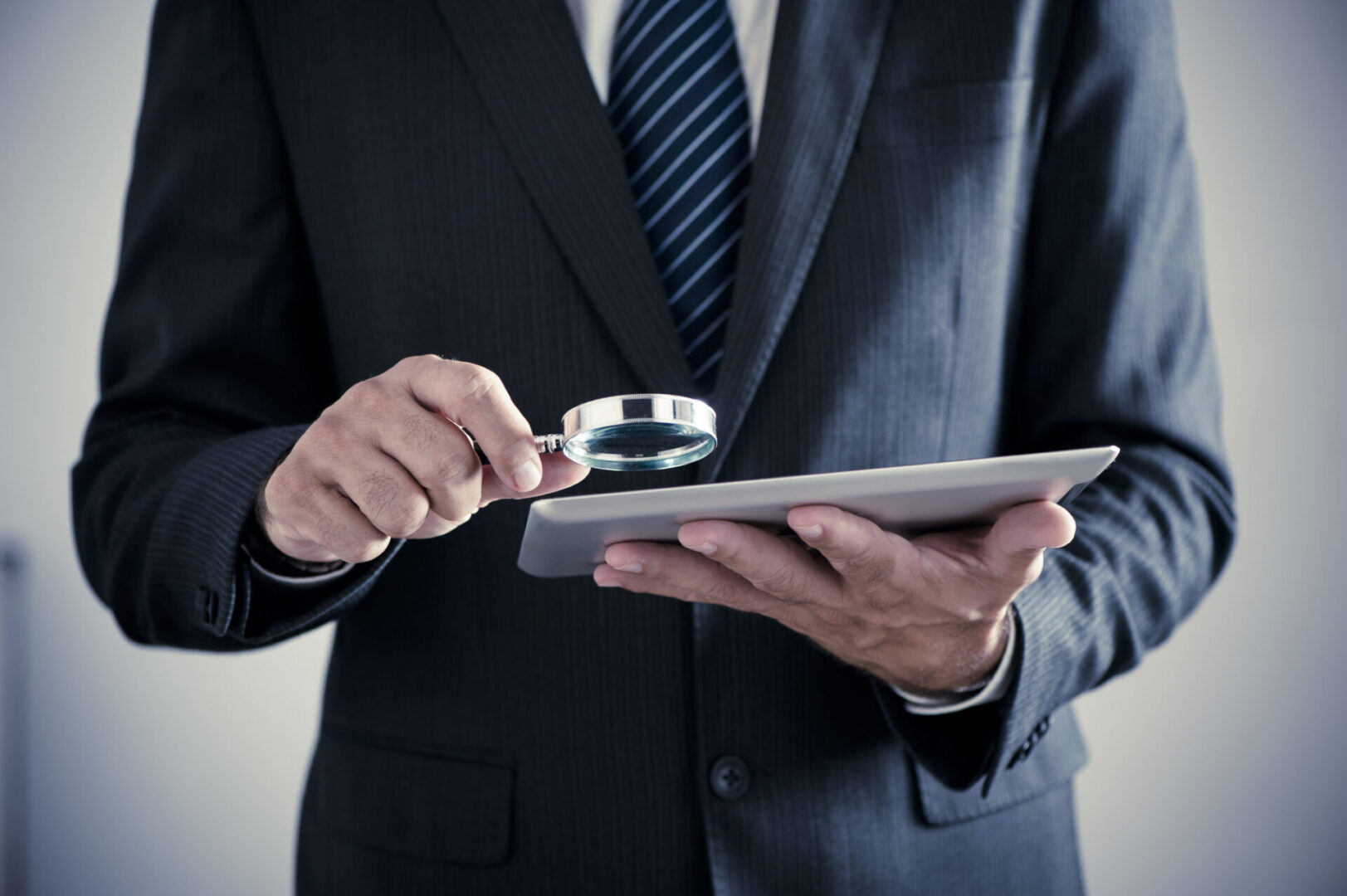 Businessman examining tablet with magnifying glass